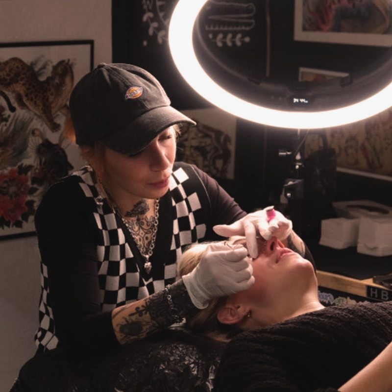 Ein Foto von Mona Hozzel der Geschäftsführerin von Heart and Poke, während sie Sommersprossen Tattoos sticht, von vorne fotografiert.