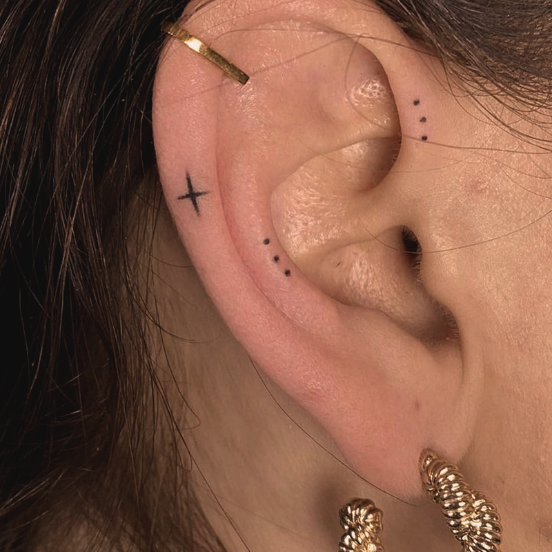 Man sieht ein Ohr einer Frau mit einem Stern und Punkte Handpoke Tattoo