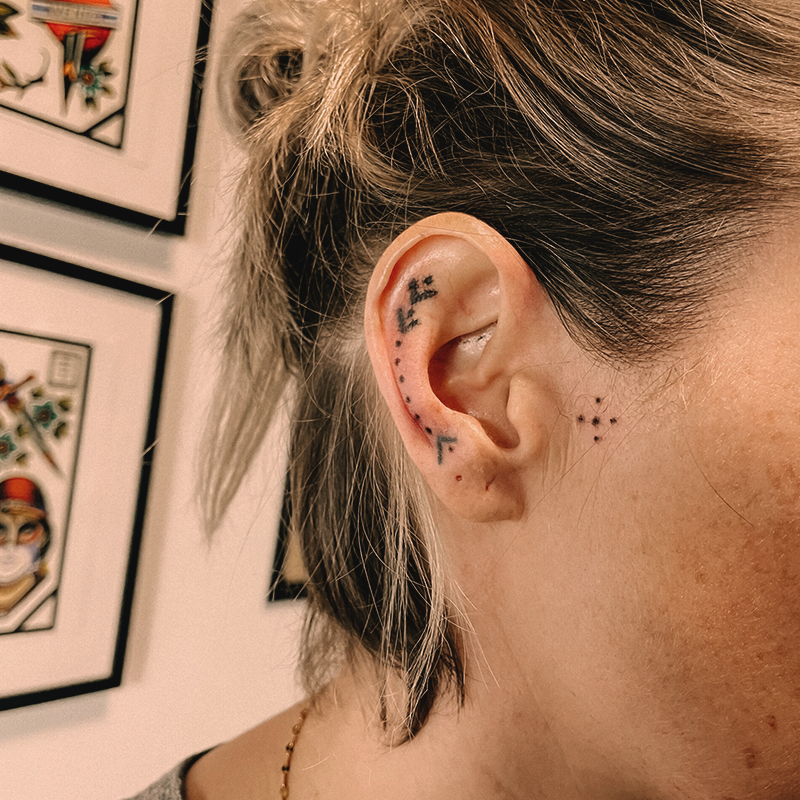 Man sieht ein Ohr einer Frau mit einem pflanzen Handpoke Tattoo